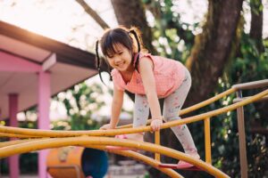 Young girl climbing on playground equipment, representing the curiosity and unique experiences of a neurodivergent child.
